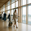 Zwangere vrouw met handbagage en instapkaart loopt rustig door een moderne Europese luchthaven, in helder daglicht vlak voor haar vlucht.