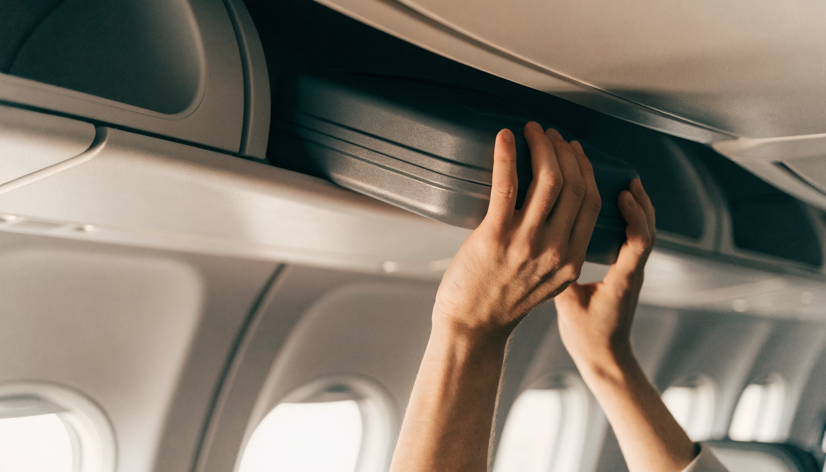 Viaggiatore solleva un trolley da cabina compatto nella cappelliera dell'aereo