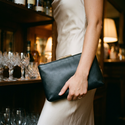 Elegante vrouw houdt een zwarte leren clutch vast bij een chique avondsetting, met zachte verlichting en feestelijke sfeer op de achtergrond.